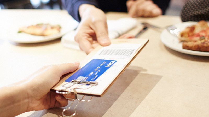Hand holding a restaurant bill with a Visa credit card.