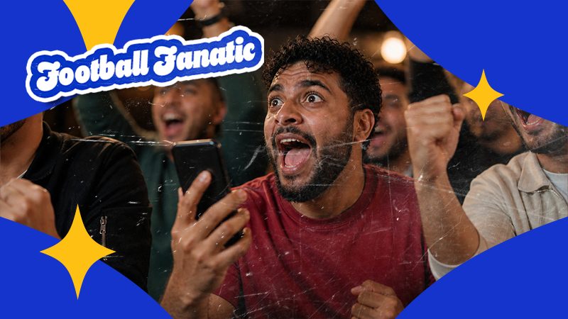 A man in a red shirt excitedly watches a football game on his phone, surrounded by cheering fans. 